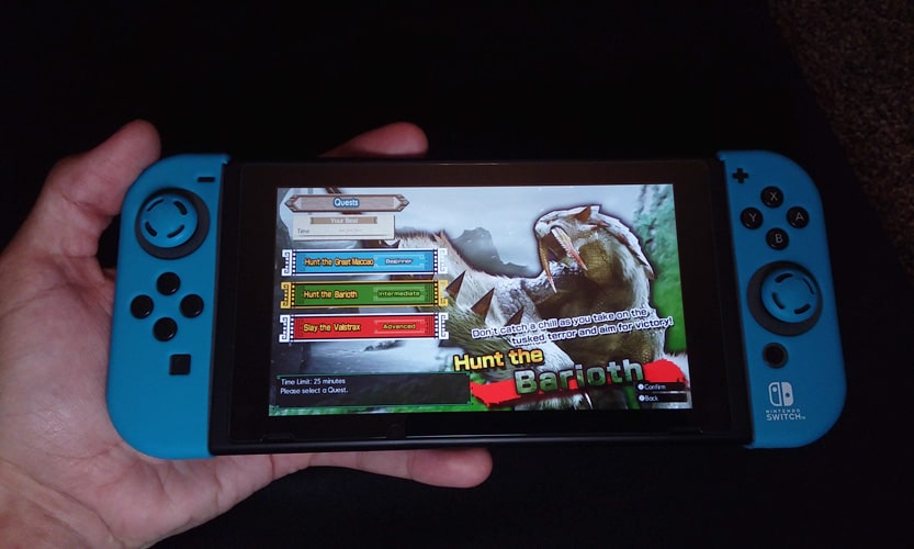 A hand holding a Switch with Monster Hunter on the screen